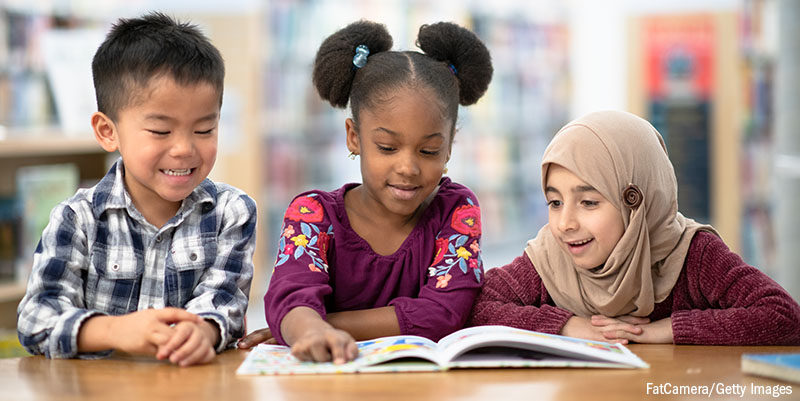 3 kids looking at a single book in the library.