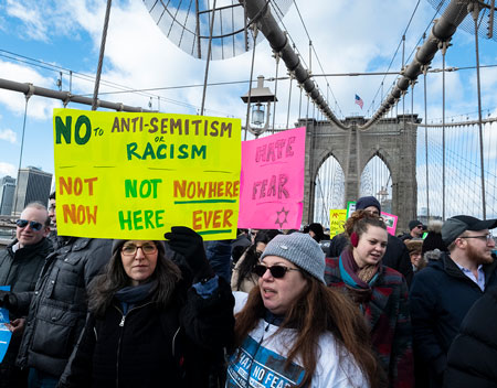 MANHATTAN, NY - JANUARY 05: A marcher walking across the Brooklyn Bridge carrying a sign of